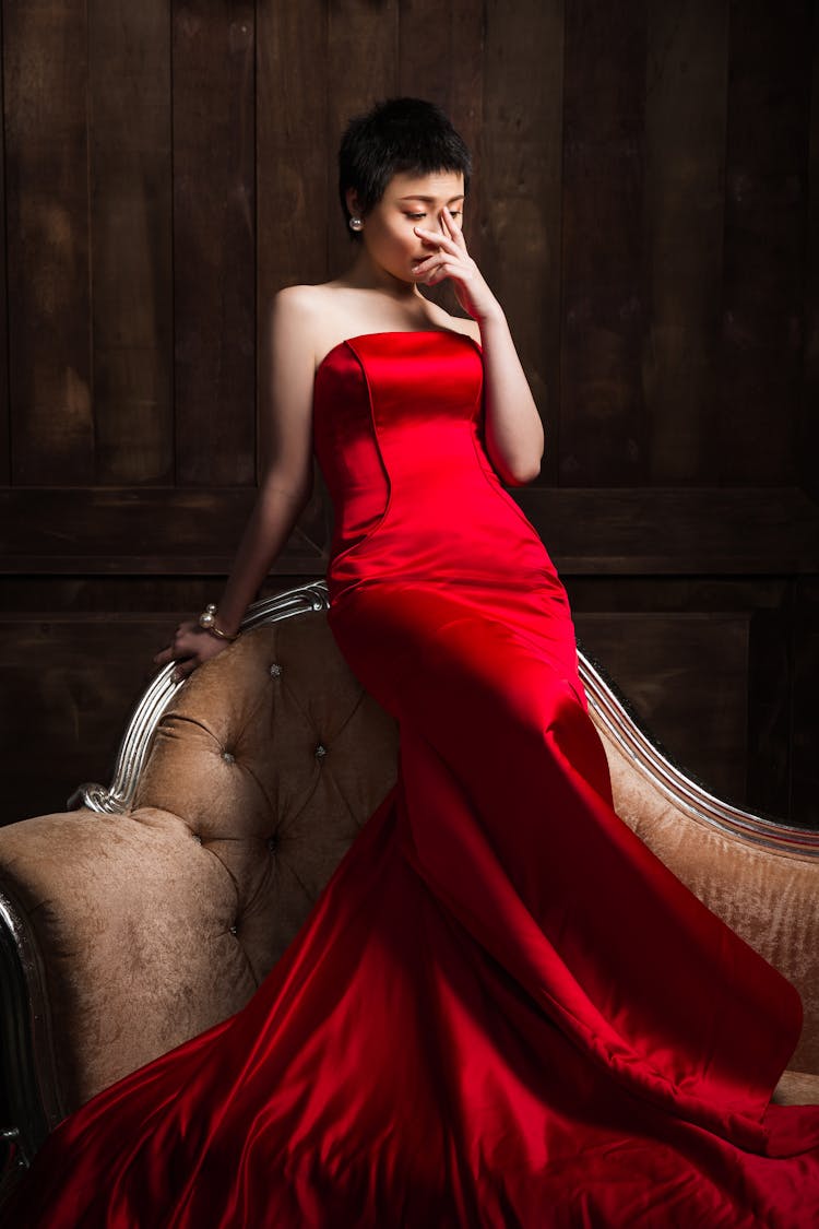 Elegant Dreamy Asian Woman In Red Dress On Couch