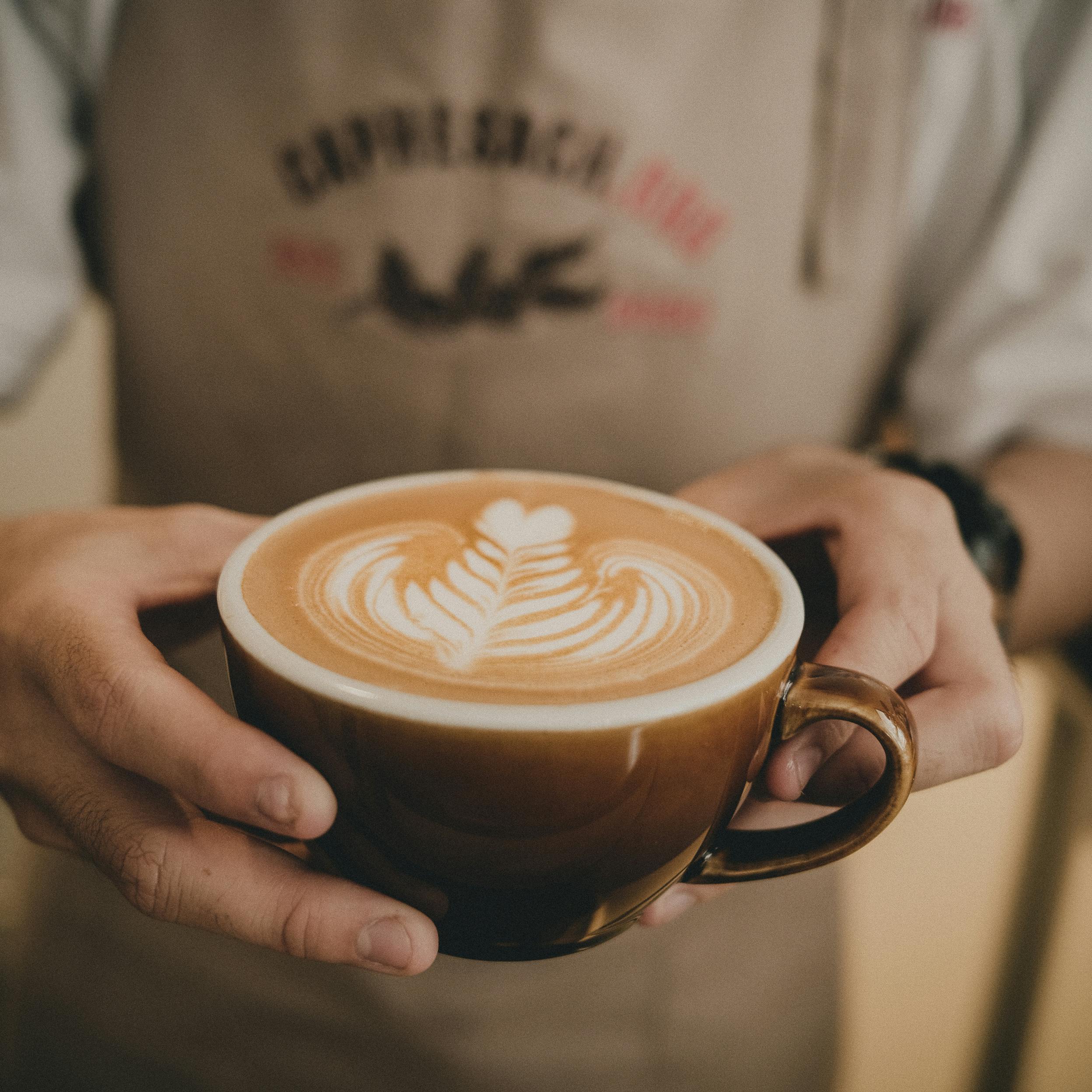 High angle of ceramic cup of coffee with picture in hands of crop unrecognizable bartender in coffee shop