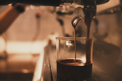 Aromatic brewed coffee pouring into glass cup from modern coffee maker in coffee shop