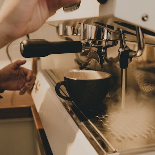 Free Side view of crop anonymous professional barista making coffee on professional equipment in coffee shop Stock Photo