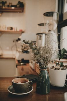 Ceramic cup of hot aromatic brewed coffee served near vase with dried plants in cozy cafe