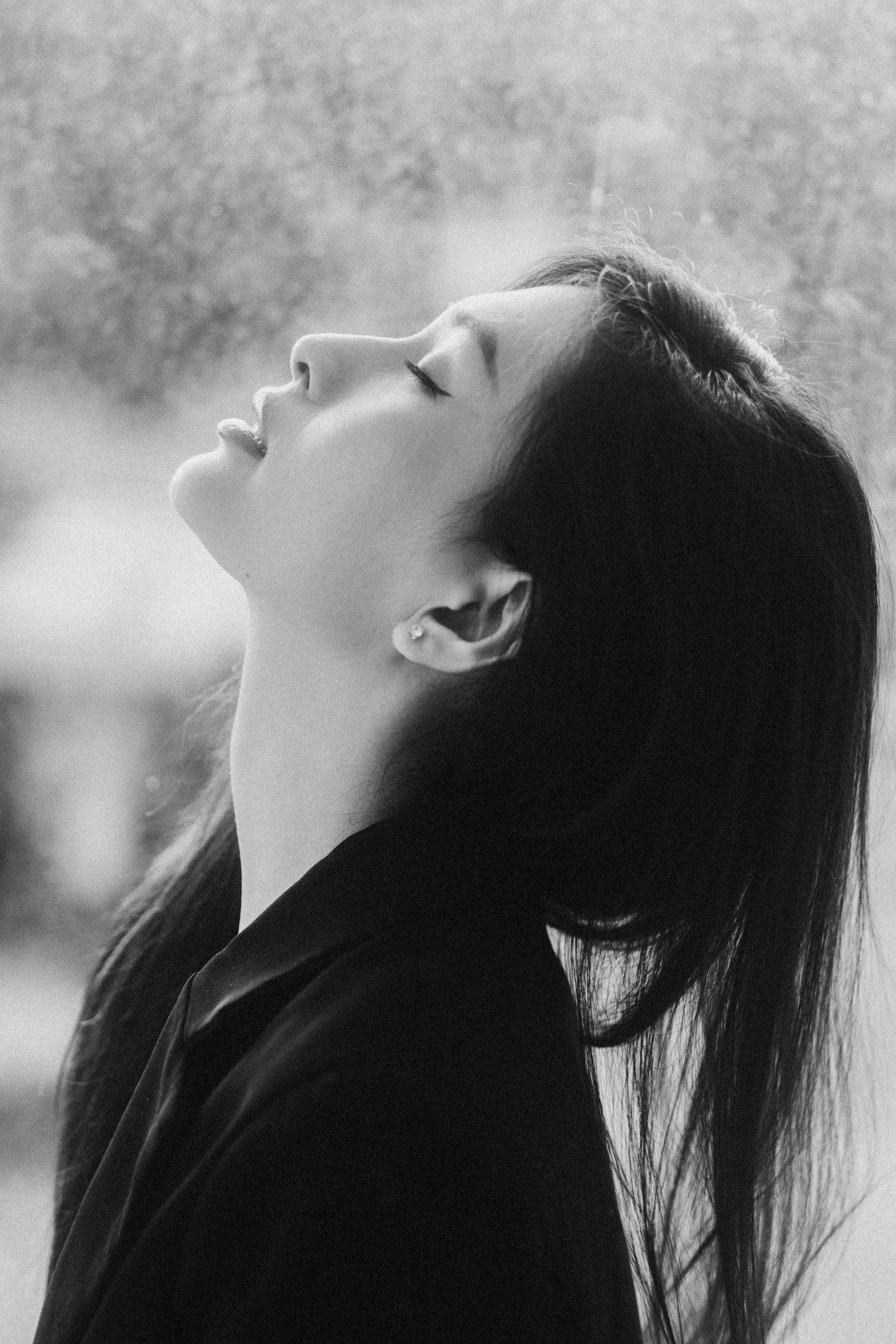 Black and white side view of young reflective female in trendy wear standing with closed eyes