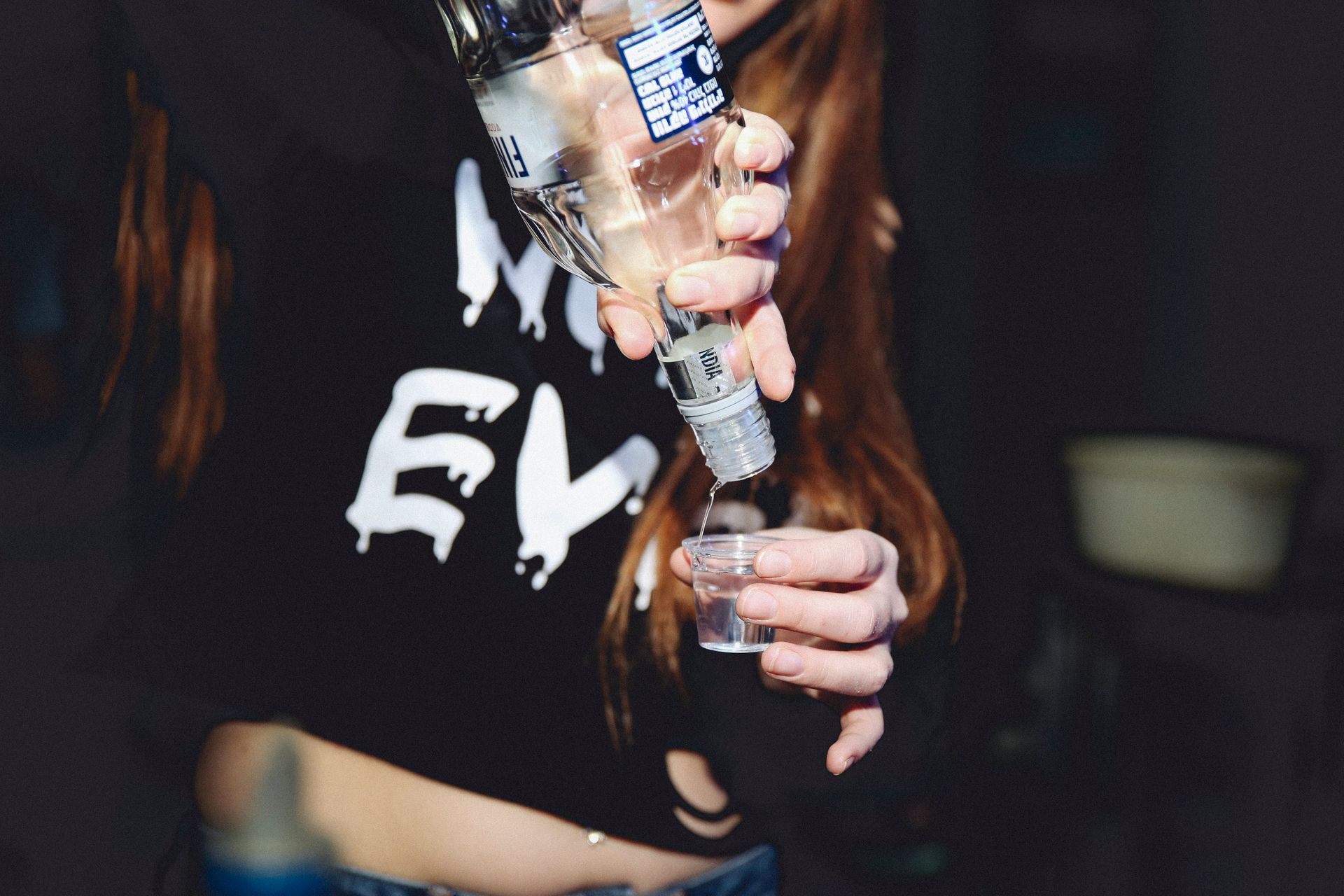 A woman pours vodka into a shot glass during a night gathering, symbolizing nightlife and celebration.