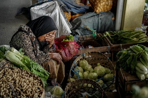 Woman Wearing a Headscarf Sitting Beside Vegetables