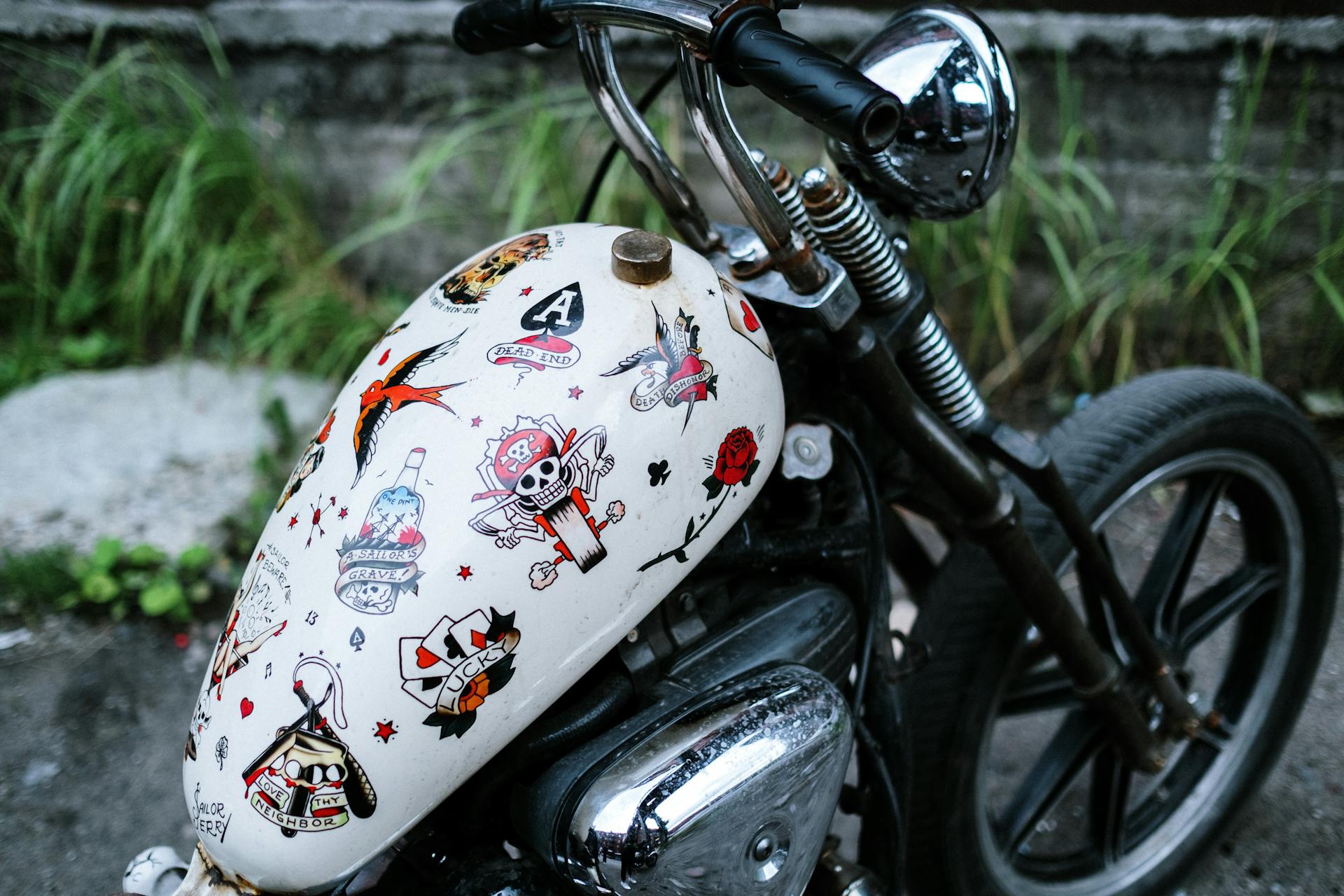 Close-up of a vintage motorcycle with a decorated gas tank parked outdoors.