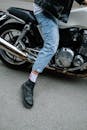 摩托车手穿着牛仔裤和皮夹克，靠在摩托车上的特写
