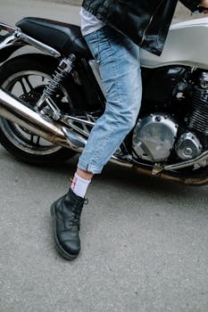 摩托车手穿着牛仔裤和皮夹克，靠在摩托车上的特写
