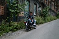 一名男子随意地坐在废弃建筑附近，骑着摩托车，散发着一种凉爽的都市气息