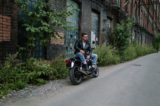 一名男子随意地坐在废弃建筑附近，骑着摩托车，散发着一种凉爽的都市气息
