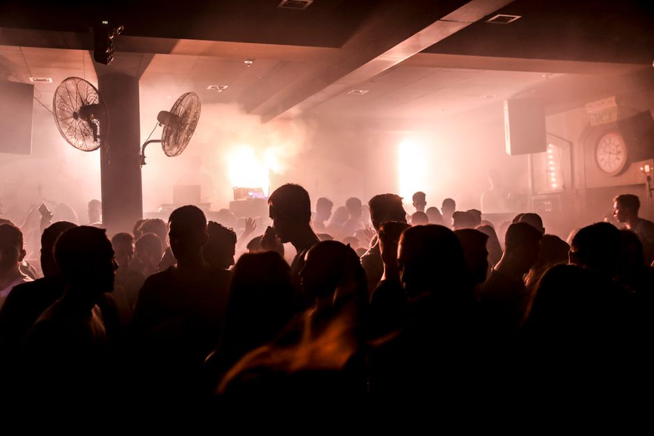 Silhouetted crowd dancing in a smoky nightclub with vibrant lights.