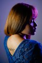 Side view of attractive female profile wearing blue blouse with hieroglyphs on back standing in studio under neon light against wall