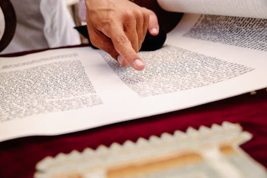 A close-up view of a hand pointing to text on an ancient religious scroll, indicating reading and study.