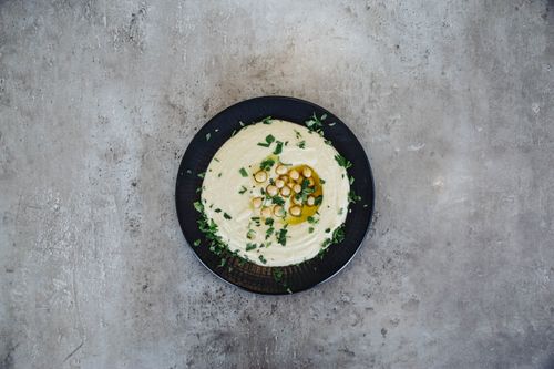 Free A flat lay of a plate of hummus garnished with chickpeas and herbs on a gray background. Stock Photo