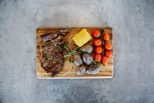 Top view of grilled steak with corn and tomatoes on a cutting board, perfect for food lovers.