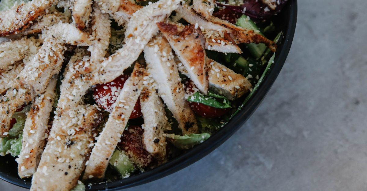 Close-up of a high-protein bowl with grilled chicken, quinoa, avocado, and edamame, garnished with sesame seeds, modern plating style