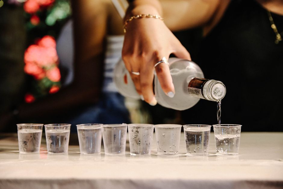 Close-up of a woman pouring vodka into shot glasses during a festive party setting.