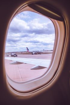 A scenic view through an airplane window showing planes on the tarmac under a cloudy sky.