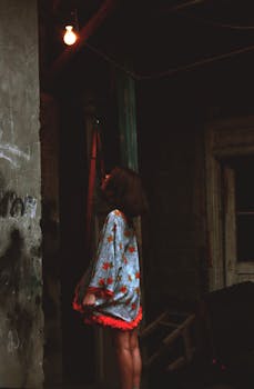 在昏暗的艺术环境中，一位穿着花裙的年轻女子凝视着灯泡