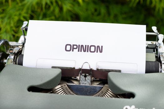Close-up of a typewriter with paper showing the word 'Opinion' outdoors.
