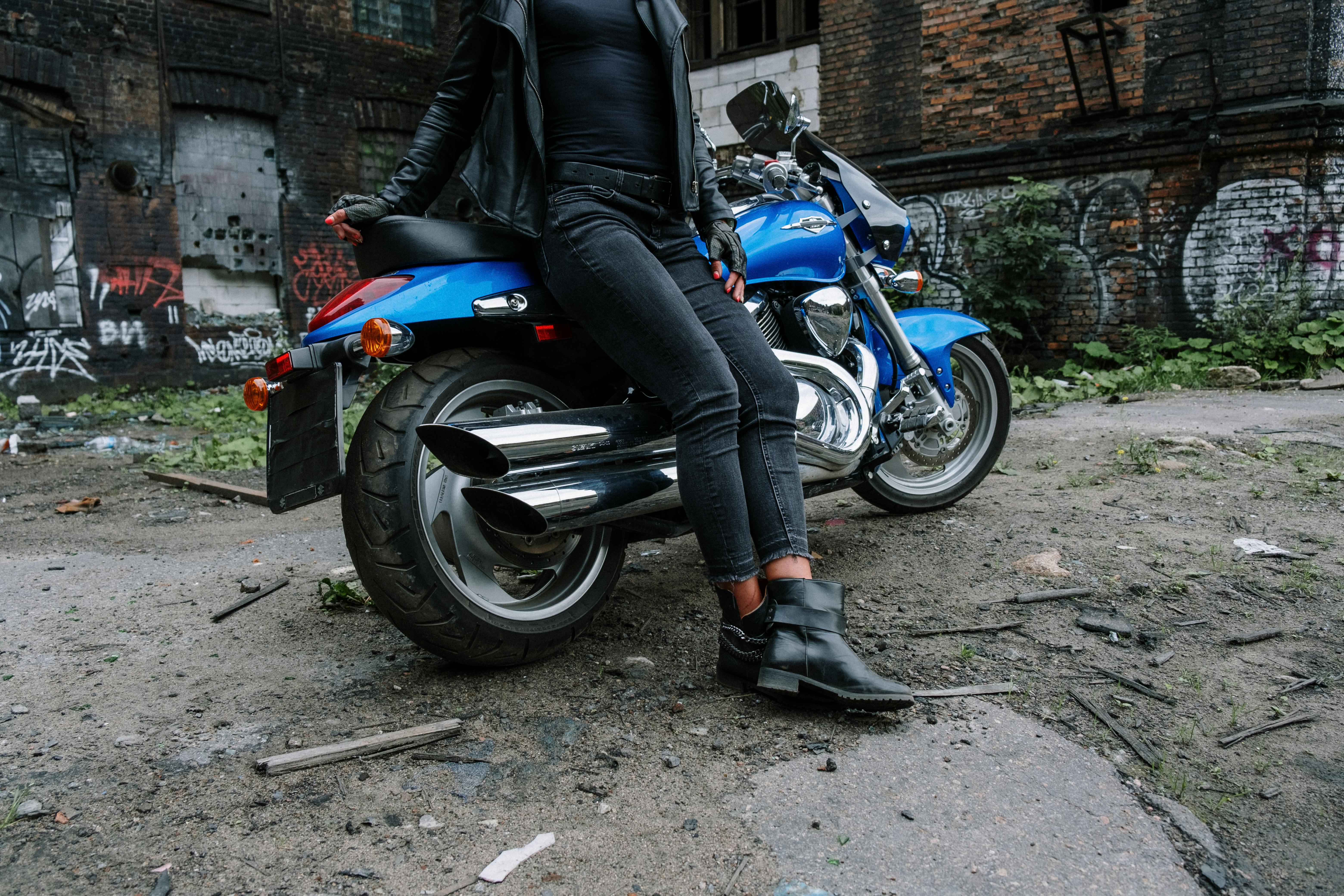 Motorcyclist in leather by a blue bike in an abandoned urban area.