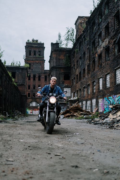 Man in Denim Jacket Riding Motorcycle Near the Abandoned Building