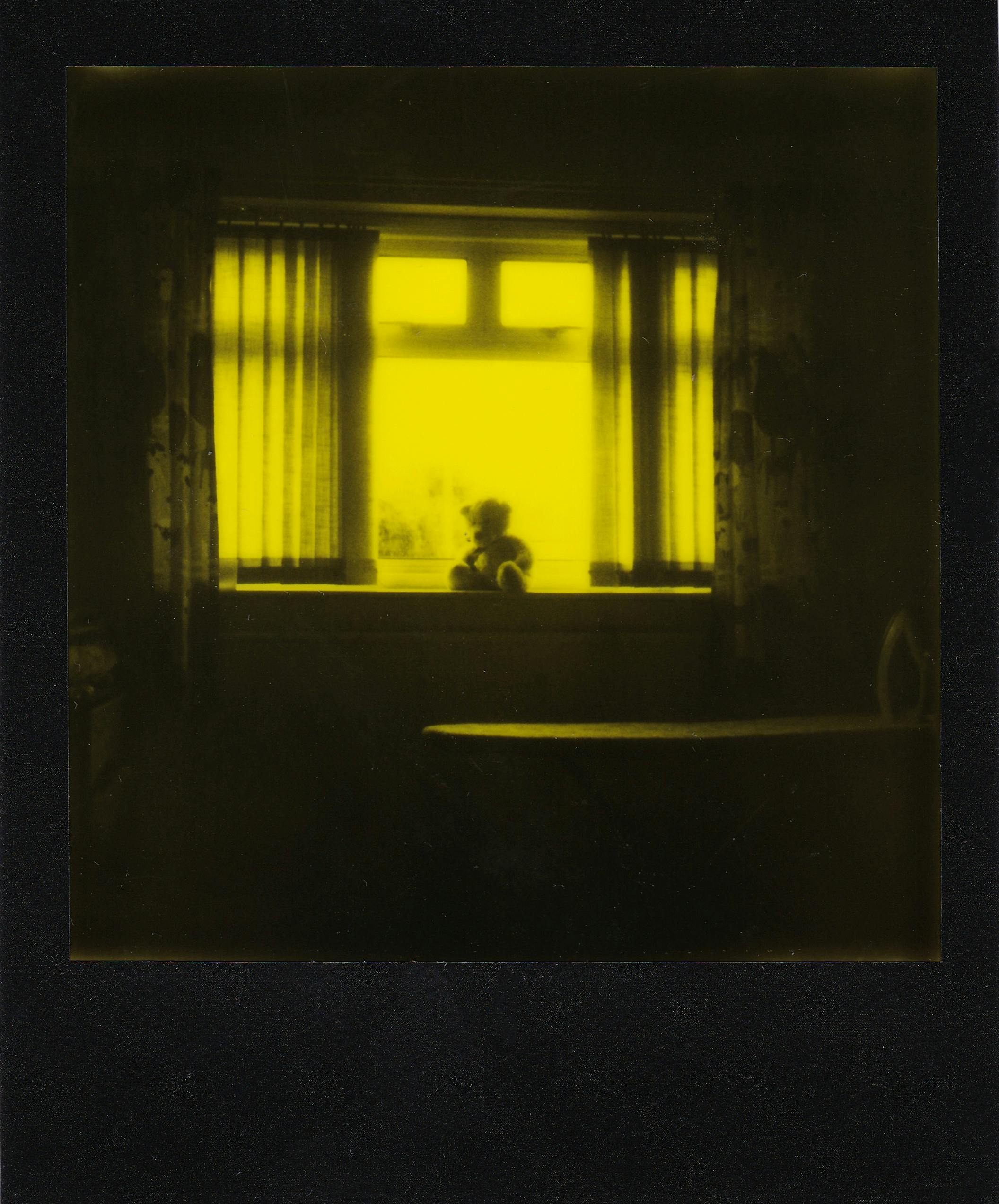 A moody room with curtains framing a teddy bear on a windowsill.