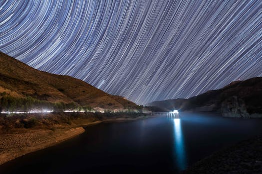 A mesmerizing long exposure capturing star trails over a serene lake and hills in Spain.