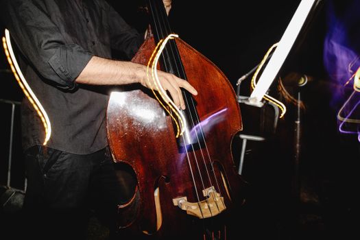Close-up of hands playing a double bass at night with artistic light trails.