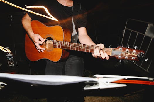 Musician strumming an acoustic Tacoma guitar outdoors at night.