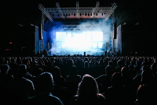 A night crowd facing a lit outdoor stage — photo by Maor Attias on Pexels