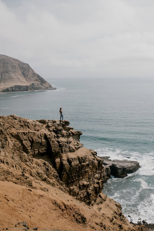 A Woman Standing on a Cliff with a View of the Ocean
