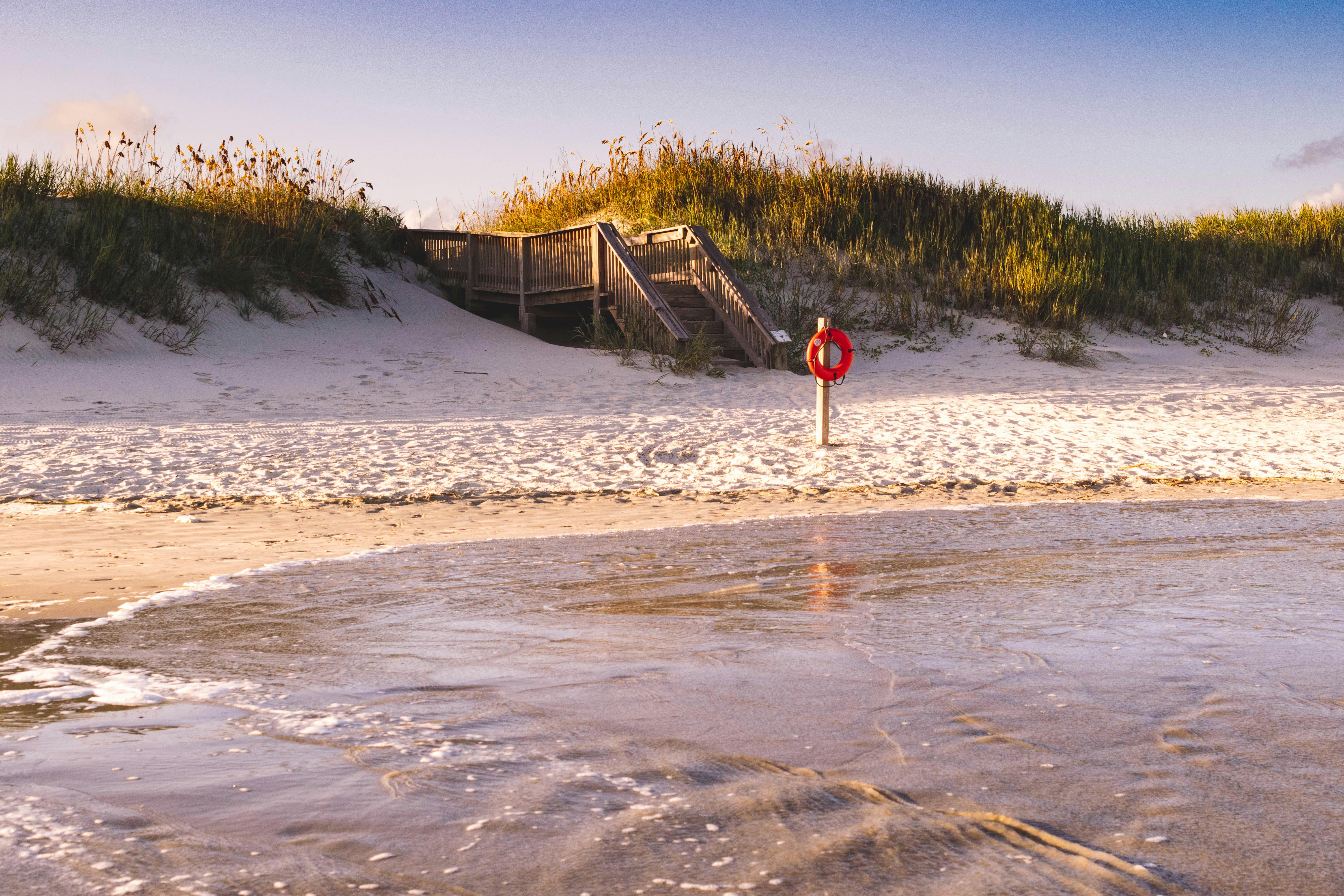 Peaceful beach scene at Sunset Beach, NC with lifebuoy and wooden stairs.