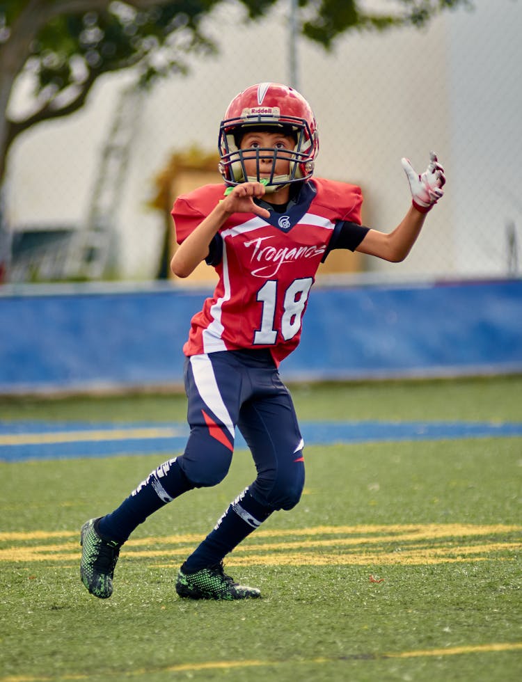 Young Football Player In Red And Blue Sports Uniform Catching The Ball