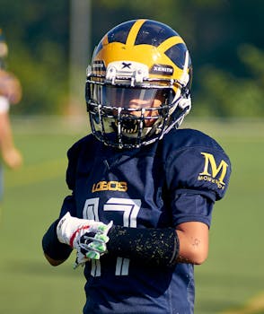A young American football player in full uniform and helmet on the field, focused and ready.