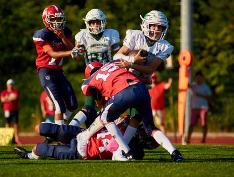 Dynamic action shot of young football players tackling during a game in bright sunlight.