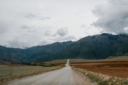 Empty road leading towards high mountains with clouds above