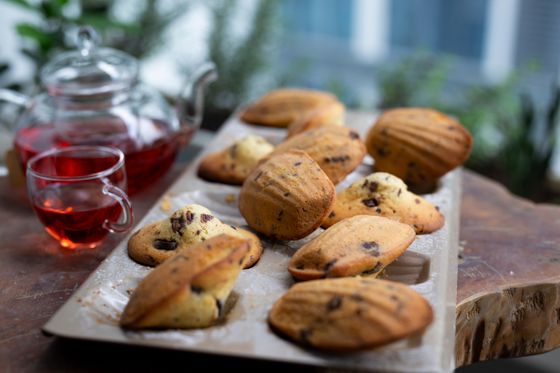 Madeleines with chocolate chips in a baking tray beside a glass teapot of red tea