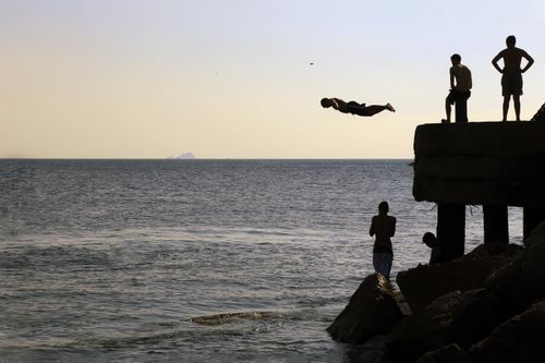 Free Silhouette of people diving into the sea at sunset by a rocky İstanbul shore. Stock Photo