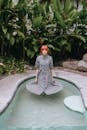 Phlegmatic young female in gray dress standing calmly in swimming pool with skirt floating on water surface in exotic resort