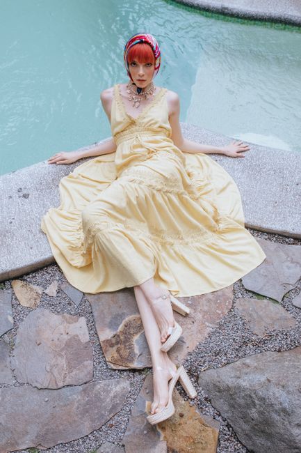 From above full body gorgeous female in yellow maxi dress and silk headscarf lying graciously on stone poolside and looking at camera