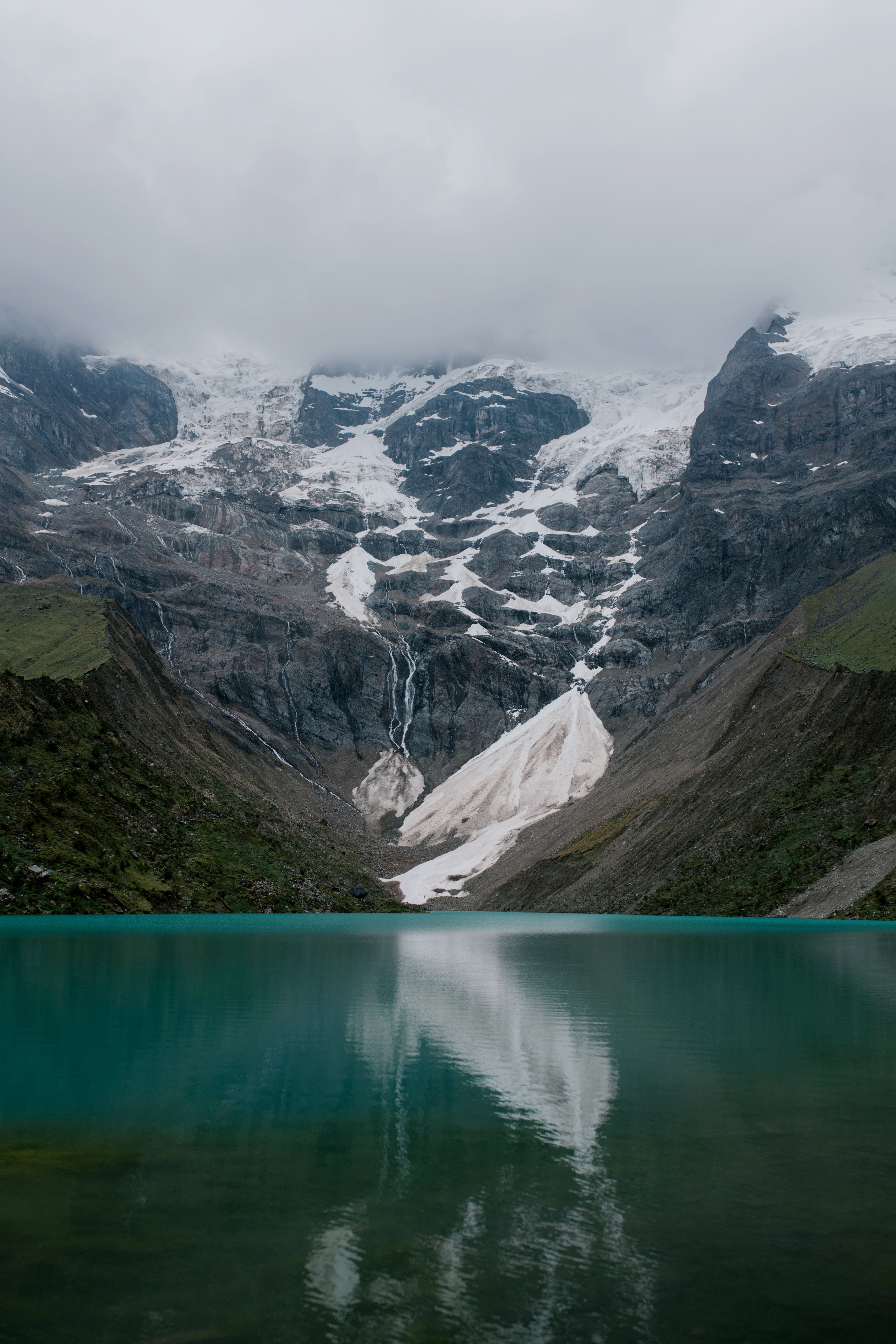 在多云的天空下，乌曼泰湖映照出白雪皑皑的安第斯山脉，景色令人惊叹