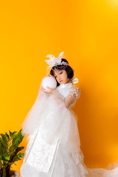 一位身着白色连衣裙、头戴羽毛饰品的年轻女孩，在充满活力的橙色背景下手持一个球