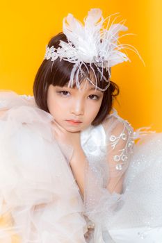 孩子身穿精致的白色服装，头戴羽毛头饰，背景是充满活力的黄色