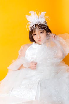 Beautiful portrait of a girl in a white dress with a feather headdress on bright yellow background.
