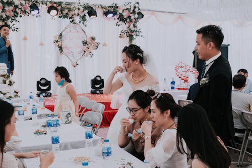 Young ethnic bride with groom and guests in elegant tent drinking together while toasting