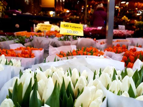 Colorful tulips on display at a market with vibrant signs, showcasing floral beauty.