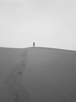 A solitary figure stands atop vast sand dunes, epitomizing isolation and wanderlust.
