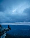 Man in Black Shirt Sitting on Rock Formation Under Cloudy Sky