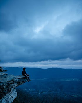 Person sits on a cliff edge with a dramatic sky and landscape view, perfect for adventure themes.