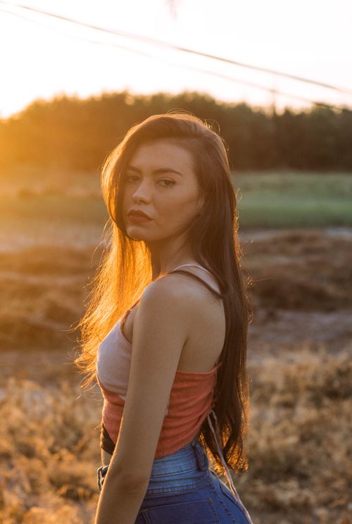 Free Side view of young contemplative female in stylish apparel looking at camera on lawn at sunset Stock Photo